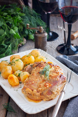Baked turkey thigh meat with potatoes on a wooden table and glasses of red wine, selective focus