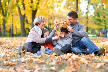 Happy family sit in autumn city park on fallen leaves. Children and parents posing, smiling, playing and having fun. Bright yellow trees.