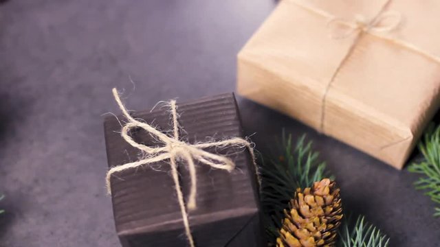 Black and brown paper christmas gift box with pine branches on dark texture surface.
