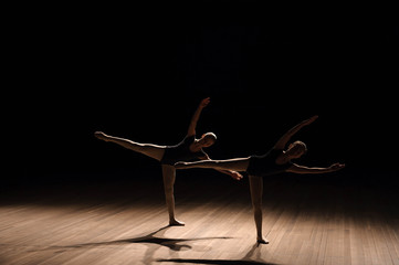 Flexible ballerinas stretch on a dark lighted scene