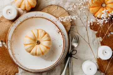 Top view on a decorated table setting for Thanksgiving dinner. Autumn ornate, white pumpkin on...