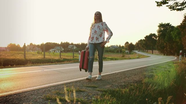 Cheerful woman with suitcase walking on road.