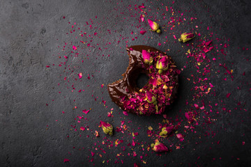 baked chocolate donut with chocolate and dried rose topping, top view, dark background