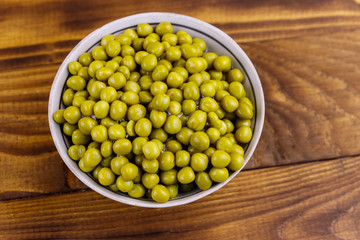 Bowl with canned green peas  on wooden table. Top view