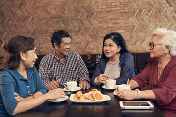 Group of senior Vietnamese people drinking tea with sweets and chatting in cafe