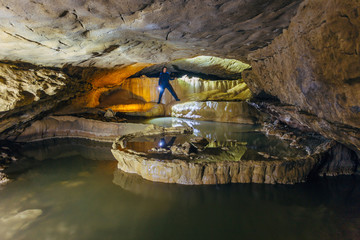 Man tourist speleologist in wetsuit with flashlight in beautiful natural cave with cascades of underground lakes in Nizhneshakuranskaya cave, Abkhazia, Georgia