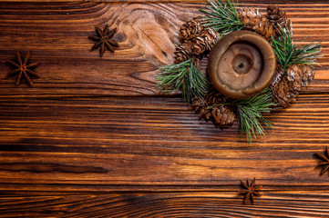 Top view, flat lay. Brown candle decorated with a fir branch with small cones. Star-shaped anise fruits are located nearby. Brown wooden boards on the background. Copy space.