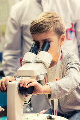 Small boy analyzing computer part while looking through microscope.