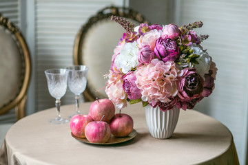 Dining table with classic chairs, a bouquet of hydrangea and peonies in a vase, wine glasses and apples