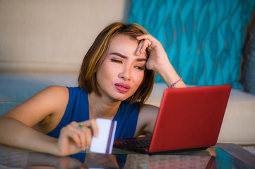 lifestyle portrait of young attractive and upset woman at home couch checking finance with credit card and laptop computer worried and stressed suffering money problem