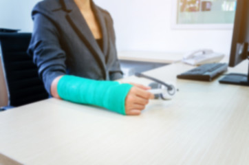 blurred woman with broken hand and green cast  working on computer in office