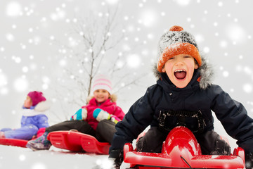 Fototapeta na wymiar childhood, sledging and season concept - group of happy little kids sliding on sleds in winter