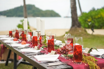 Decorating the table in the open air, on the sea. Wedding dinner in burgundy and red tones. Details - grapes, pomegranate, candles, green fern leaves