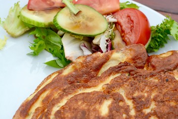 Golden cooked omelette with side salad served on a white plate 