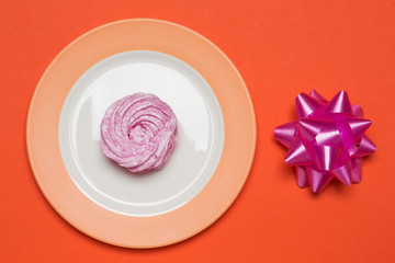 plate with dessert on an orange background, near a lilac bow, the concept of children's birthday, a cheerful holiday