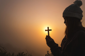 Silhouette of woman hands praying with cross  in nature sunrise background,  Crucifix, Symbol of...