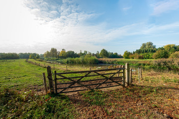 Fototapeta na wymiar Wooden gate between two wooden beams closed with a rusty chain in the foreground of grassland along the Dutch river Mark