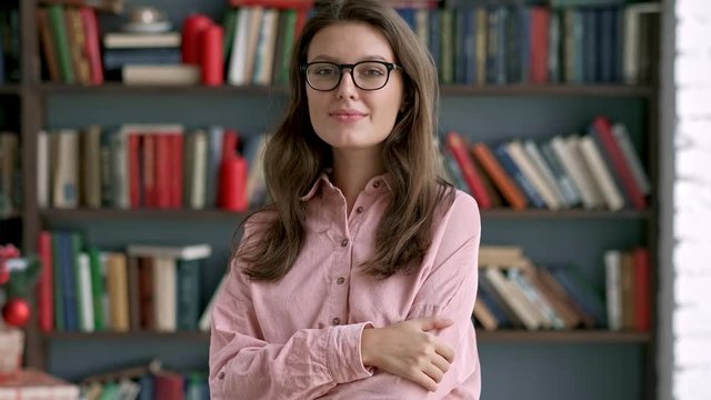close up portrait of young pretty librarian woman smiling happy looking at camera in library bookshelf background knowledge learning