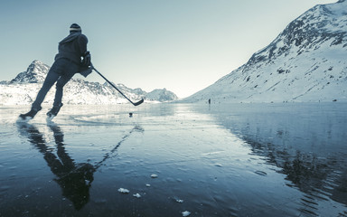 Beautiful view of the winter lake in the mountains. Clearing ice and winter mood, ice hockey player with ice skating in nature on frozen lake Lago Bianco - Switzerland