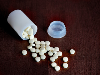 Scattered on the table white pills, overturned jar
