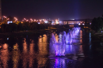 Colored luminous fountains in the middle of the lake at night.