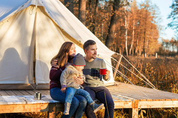 Happy family drinking coffee while sitting near canvas bell tent in a forest