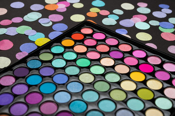 Make-up eyeshadow palette with scattered confetti on a black background.