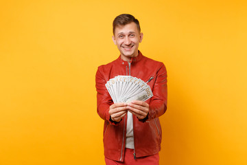 Obraz premium Portrait vogue handsome young man in red leather jacket, t-shirt holding lots of dollars banknotes, cash money isolated on bright trending yellow background. People lifestyle concept. Advertising area