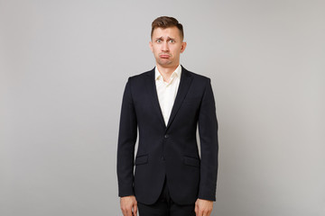 Fototapeta premium Portrait of offended inflated young business man in classic black suit, white shirt standing isolated on grey wall background in studio. Achievement career wealth business concept. Mock up copy space.