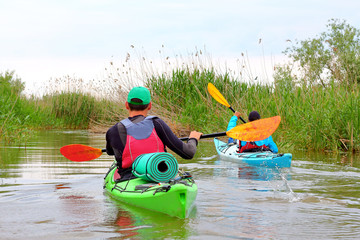 Two friends travel by kayaks in Danube river and lake on biosphere reserve in spring