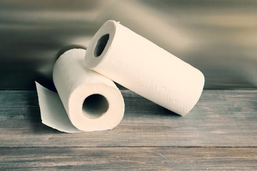 Two white paper tissue rolls - hygienic disposable products for body care, bathroom, kitchen and household on wooden table. Selective focus.. Toned. Copy space.