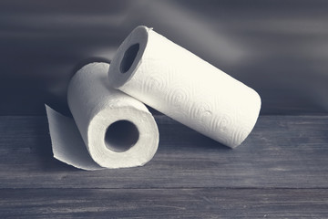 Two white paper tissue rolls - hygienic disposable products for body care, bathroom, kitchen and household on wooden table. Selective focus.. Toned. Copy space.