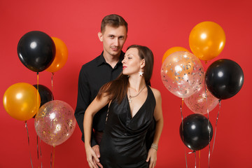 Stunning young couple in black clothes celebrating birthday holiday party isolated on bright red background air balloons. St. Valentine's International Women's Day Happy New Year 2019 concept. Mock up