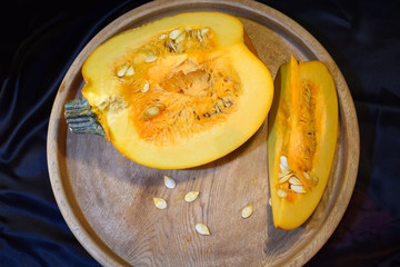 A sliced ripe pumpkin is on a large wooden dish. Black background. Selective focus.