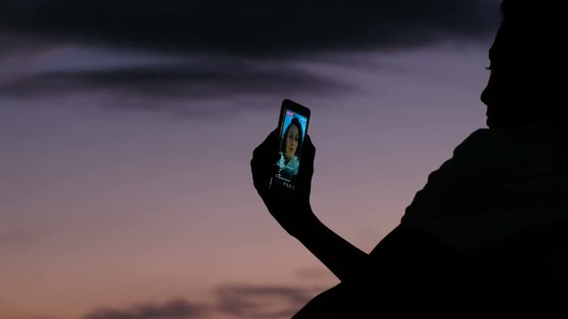 Silhouette of a girl uses a cellphone to live on social networks at sunset close-up