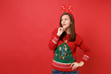 Pensive young Santa girl in fun decorative deer horns looking up, put hand prop up on chin isolated on bright red background. Happy New Year 2019 celebration holiday party concept. Mock up copy space.