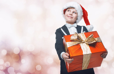 Obraz na płótnie Canvas Beautiful little boy with a big Christmas gift in a Santa Claus hat. Christmas gifts for children. Smart boy Celebrates Christmas. New Year's holidays
