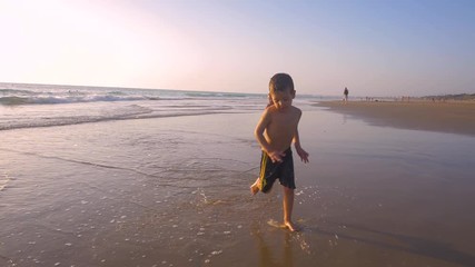 Slow motion - A child 3-5 years old running freely while the camera chase him and he laughs, in a sunny day in the beach 