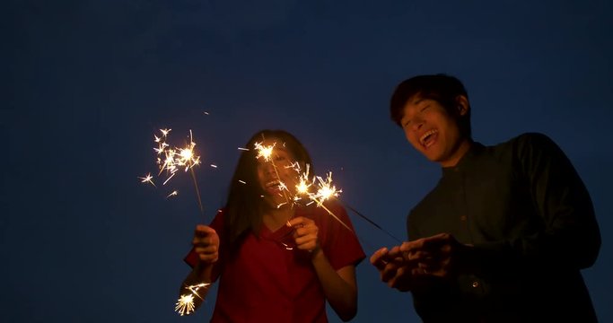 Young asian couple playing fireworks together at rooftop in slow motion.