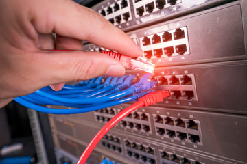 man working in network server room with fiber optic hub for digital communications and internet