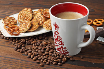 A cup of coffee, grains of coffee and cookies on a wooden table.