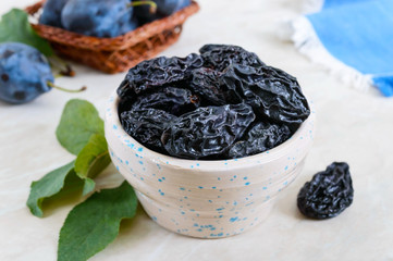 Prunes in a clay bowl and fresh plums, leaves on a table. Fresh prunes for healthy life.