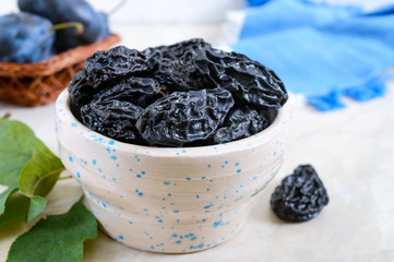 Prunes in a clay bowl and fresh plums, leaves on a table. Fresh prunes for healthy life.