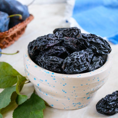 Prunes in a clay bowl and fresh plums, leaves on a table. Fresh prunes for healthy life.
