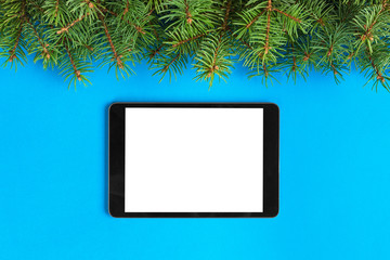 Tablet with blank screen on the blue pastel color background. Top view with christmas decor