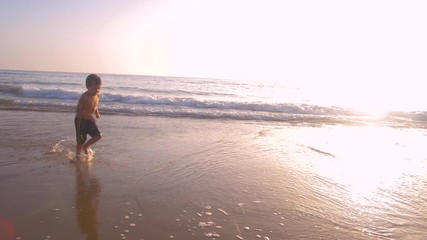 Slow motion - A child 3-5 years old running freely while the camera chase him and he laughs, in a sunny day in the beach 