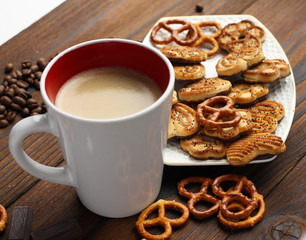 A cup of coffee, grains of coffee and cookies on a wooden table.