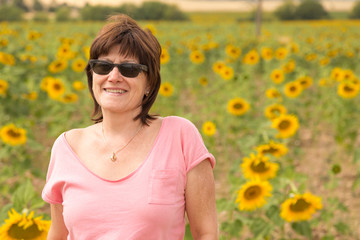 Naklejka na ściany i meble Mature woman with sunglasses in a field of sunflowers