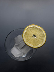 Lemon slice on glass with ice at grey background