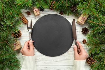 top view girl holds fork and knife in hand and is ready to eat. Empty black slate plate on wooden...